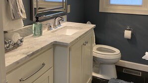 A bathroom with a white vanity, a large mirror, a sink, a toilet, and a window with frosted glass. - Newly Remodeled Midtown home 5 miles from PGA (Tulsa)