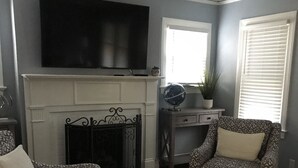 A living room with a fireplace, two patterned armchairs, a television above the fireplace, and a patterned rug. - Newly Remodeled Midtown home 5 miles from PGA (Tulsa)