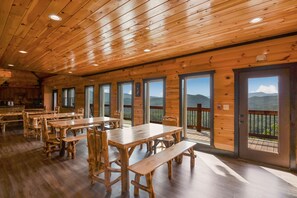 Una cabaña de madera con varias mesas y bancos para comer, ventanas amplias con vistas a la montaña y un balcón.