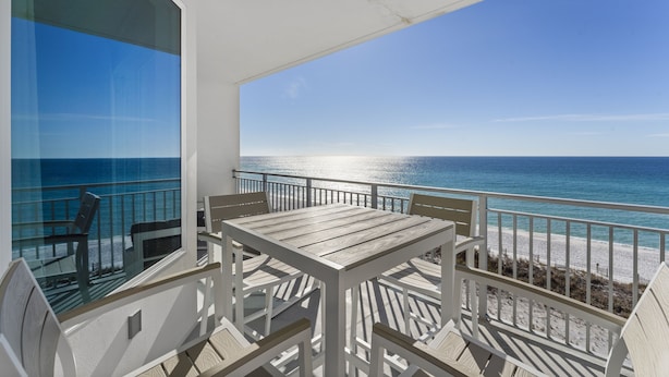 Ein Balkon mit Blick auf das Meer, einem Holztisch und weißen Stühlen.