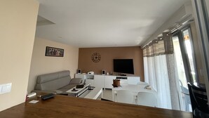 A modern living room with a sofa, a coffee table, a TV, and a dining area with chairs and a table.