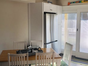 Cocina compacta con armarios blancos, un refrigerador empotrado, una mesa de comedor con sillas y un puerta corrediza de vidrio que da a un balcón.