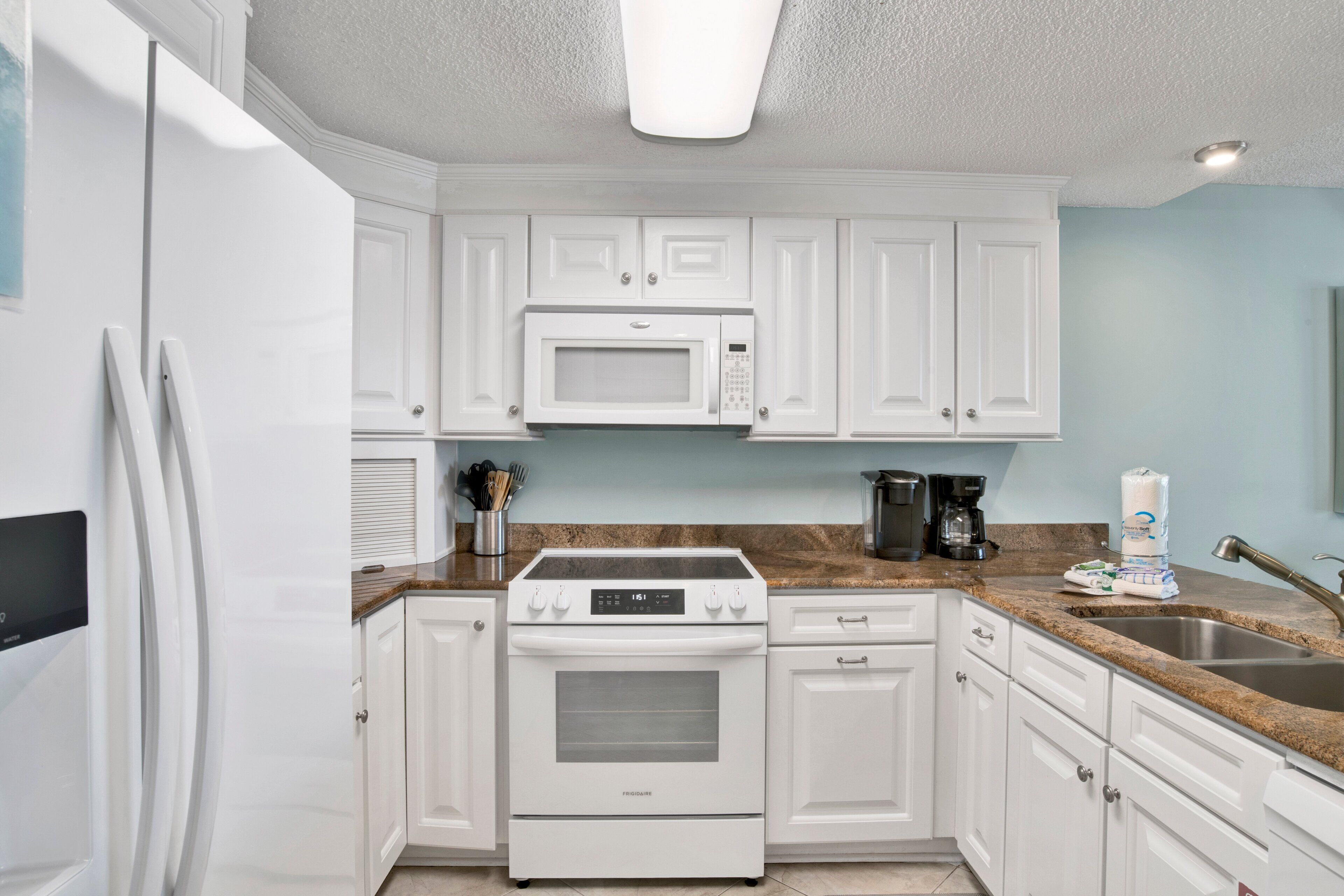 A kitchen with white cabinets, a white stove, a microwave, and a granite countertop.
