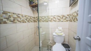 A small, tiled bathroom with a shower, toilet, and a shelf with a plant and toiletries. - 2 Guests 1Bed Studio 3min to Beach and Main Street (Sosúa)