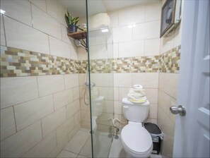 Un bagno piccolo rivestito di piastrelle, con doccia, WC e uno scaffale con una pianta e articoli da toilette.