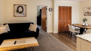 Un salon avec un canapé noir, une table basse en bois et un coin repas comprenant une table et des chaises en bois.