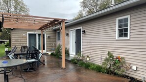 Un patio couvert avec une table et des chaises, une pergola et une maison avec une porte de garage.