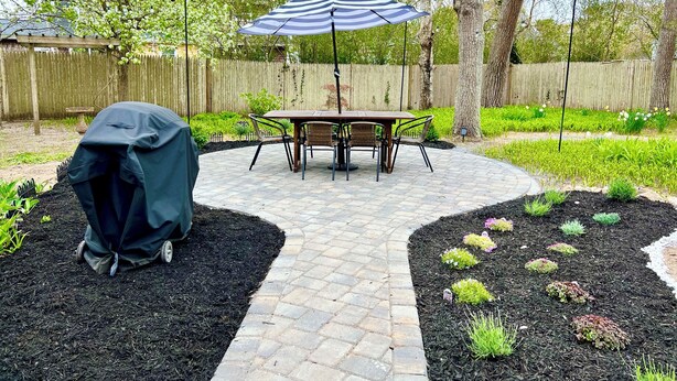 A patio with a table and chairs, a covered grill, and a striped umbrella.