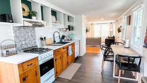 A modern kitchen with wooden cabinets, a white countertop, and a dining area with a table and chairs.