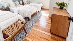 A bedroom with two beds, a wooden floor, a large window, a night sky painting, and a mirror on the wall.