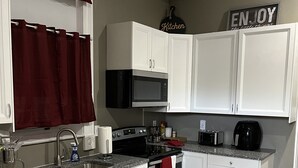 Une cuisine moderne avec des meubles blancs, un lave-vaisselle en acier inoxydable, un four à micro-ondes et une machine à café.