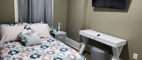 Een slaapkamer met een bed, nachtkastje, televisie, bureau en stoel.