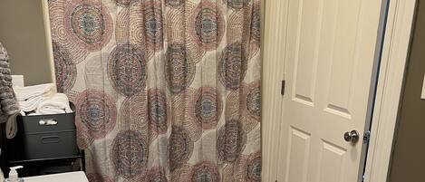 A bathroom with a white sink, a patterned shower curtain, a wooden floor, and a door with a blue stripe.