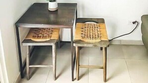 Un pequeño comedor con una mesa y dos sillas, una planta en maceta y una obra de arte enmarcada en la pared.
