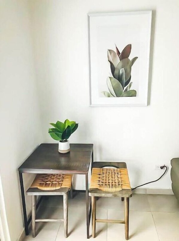 A small dining area with a table and two chairs, a potted plant, and a framed artwork on the wall.