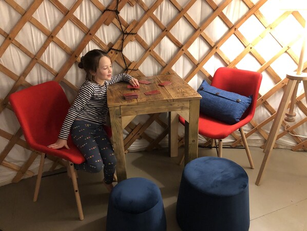 Un niño sentado a una mesa de madera con sillas rojas y azules, un otoman azul y un muro de celosía de madera al fondo.