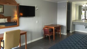 Habitación de hotel con cama, escritorio, silla, televisión en la pared y baño a la vista a través de una puerta abierta.