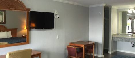 Habitación de hotel con cama, escritorio, silla, televisión en la pared y baño a la vista a través de una puerta abierta.