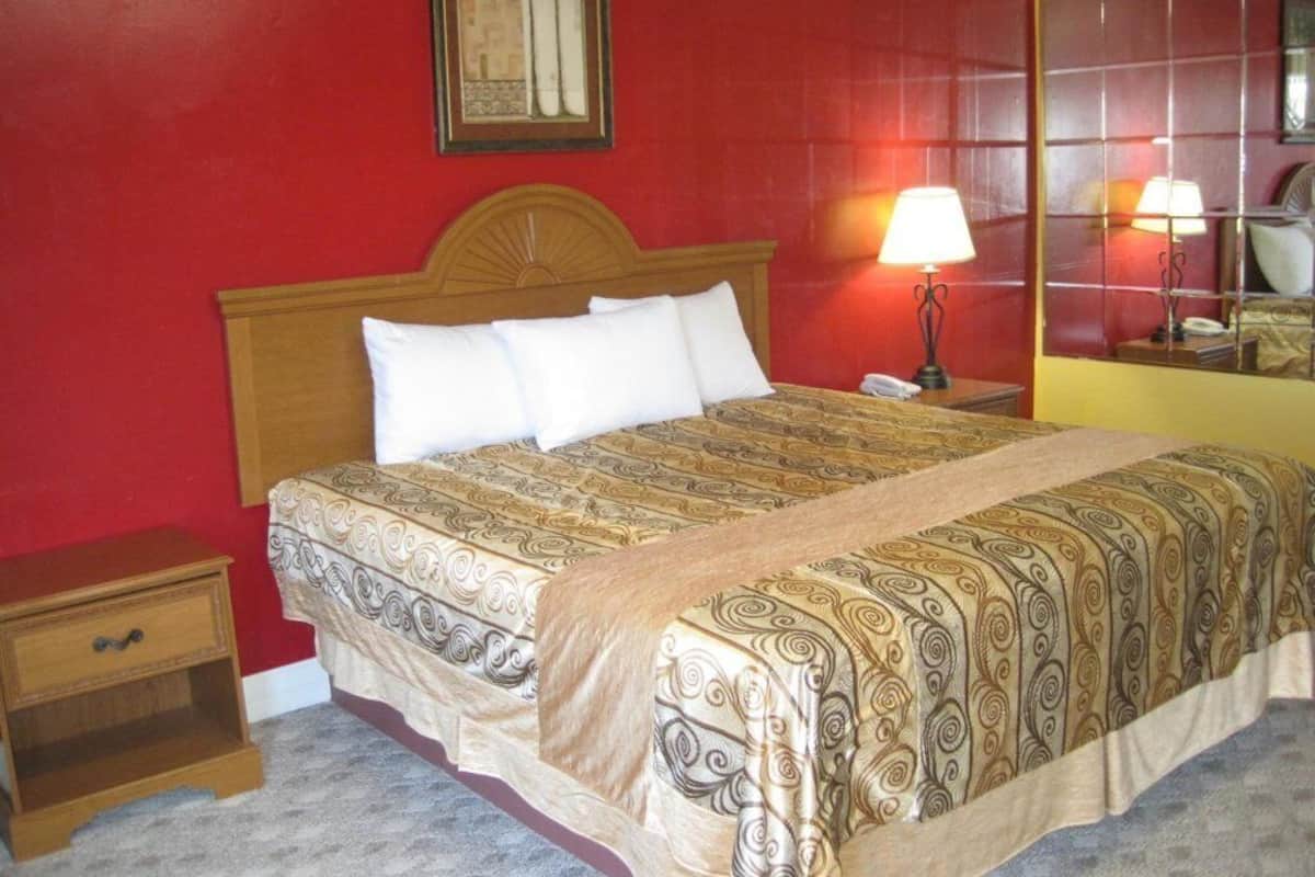 A hotel room with a large bed, a nightstand, a lamp, and a mirror on the wall.