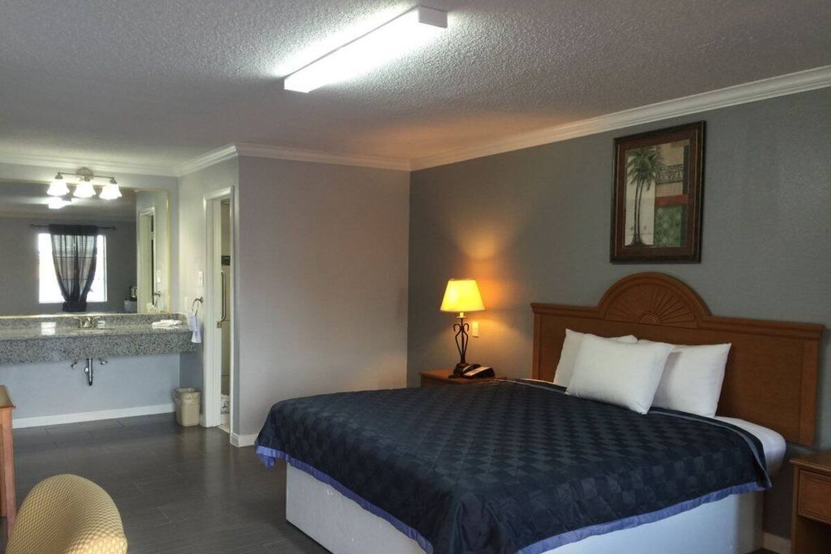 A hotel room with a bed, a nightstand, a lamp, a bathroom with a sink, and a mirror.