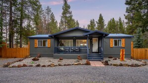 Een chalet van twee verdiepingen met een overdekte veranda, een grindpad en een houten omheining.