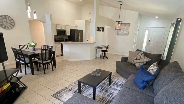 A modern living room with a grey sofa, a coffee table, and a dining area with chairs and a table. - Palm Tree Fairways (Haines City)