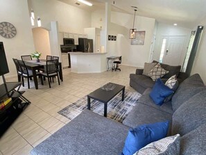 Ein modernes Wohnzimmer mit einem grauen Sofa, einem Couchtisch und einem Essbereich mit Stühlen und einem Tisch.