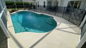A swimming pool with a curved edge, surrounded by a covered patio area with a glass railing. - Palm Tree Fairways (Haines City)