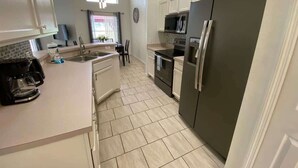 A modern kitchen with white cabinets, a stainless steel refrigerator, and a tiled floor. - Palm Tree Fairways (Haines City)