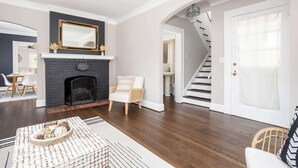 Una sala de estar con chimenea, una escalera y una puerta que da a otra habitación.