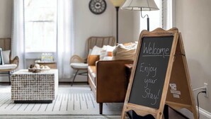 Una sala de estar acogedora con una mesa de centro de madera, un sofá y una pizarra con la inscripción 'Welcome Enjoy your Stay!'.