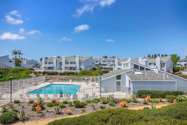 A residential area with a swimming pool surrounded by a fence, multiple apartment buildings, and landscaped gardens.