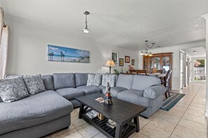 A living room with a grey sectional sofa, a dark wooden coffee table, and a painting of a beach scene on the wall.