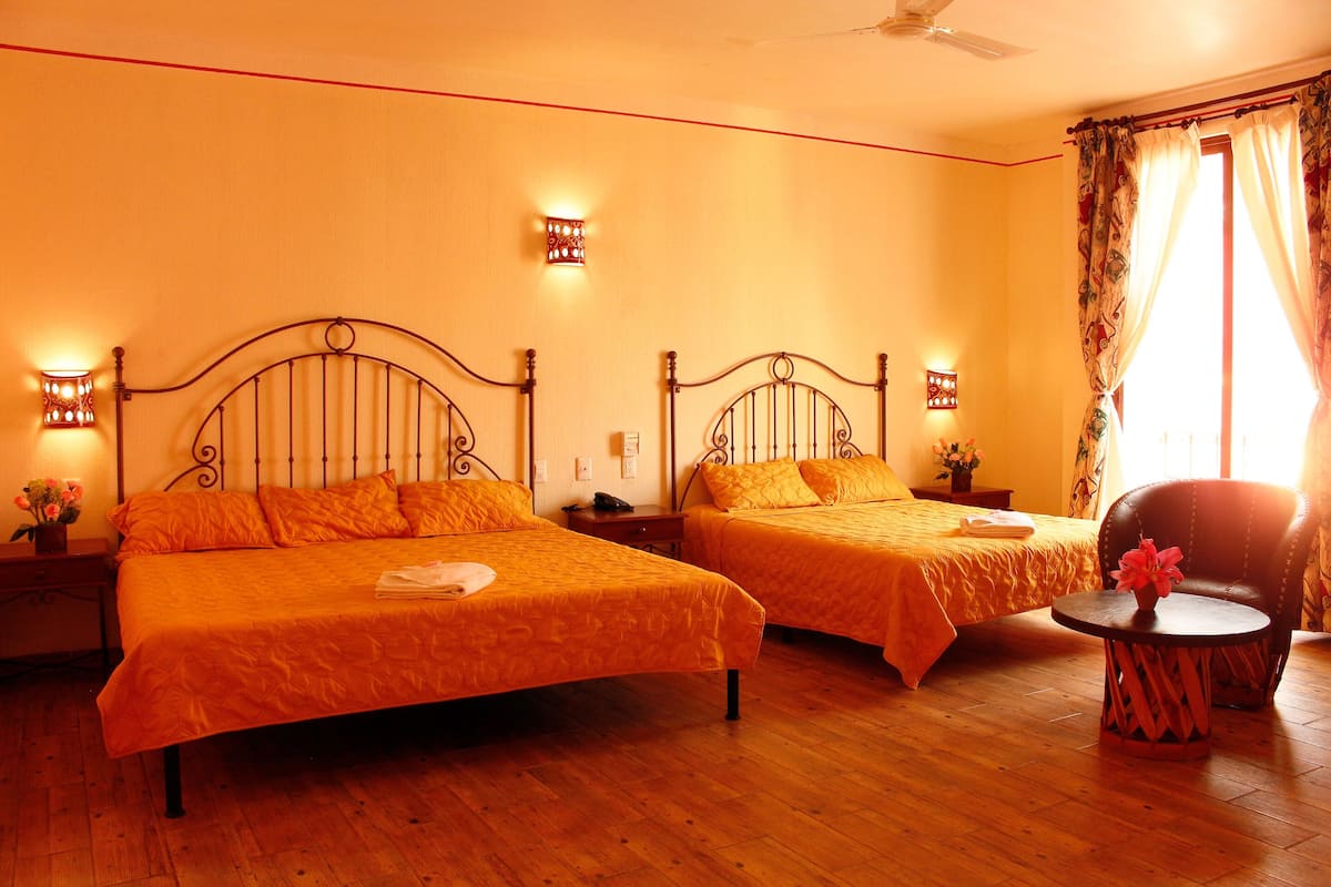 Habitación de hotel con dos camas, suelo de madera, una silla y una mesita con un florero.