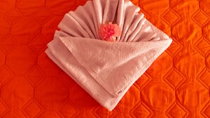 Una toalla rosa doblada con pulcritud, con una flor rosa sobre un edredón acolchado naranja.