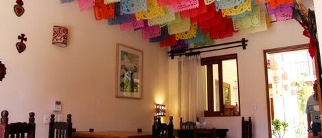 Un comedor con muebles de madera, un techo decorado con adornos de papel de colores y una puerta que da al exterior.