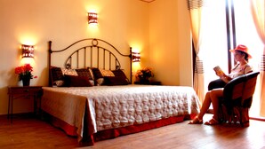 Un dormitorio con cama, mesitas de noche y un sillón de lectura junto a la ventana.