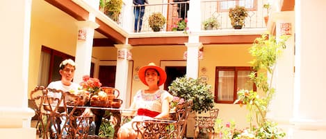 A courtyard with ornate wrought iron furniture, potted plants, and a balcony with railings.