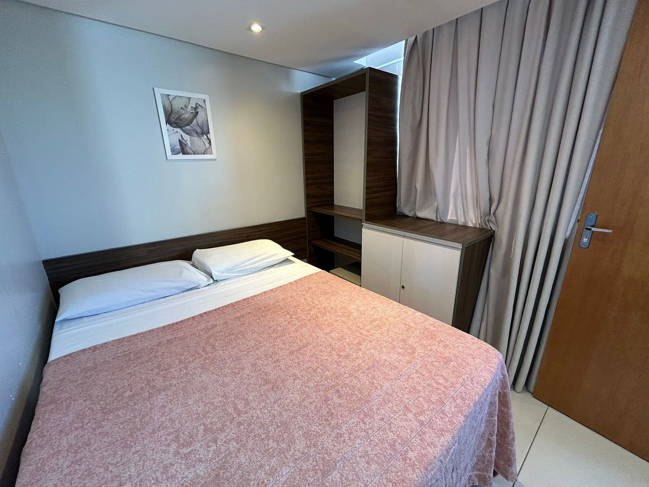 Une chambre d’hôtel avec un lit, une armoire, un miroir et une fenêtre avec des rideaux.