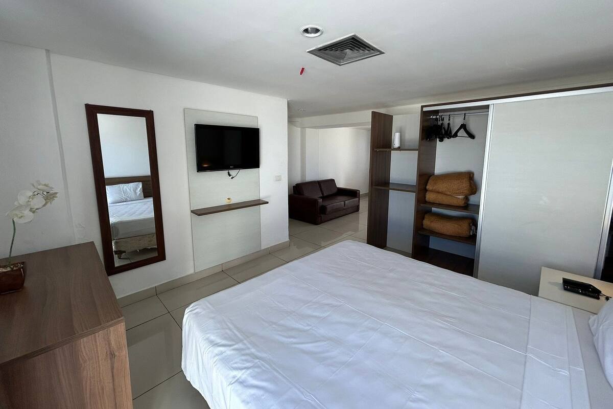 Habitación de hotel con cama, televisor montado en la pared, armario y espejo.
