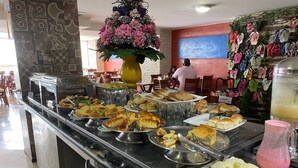 A buffet area with various food items, a decorative flower arrangement, and a wall with hanging slippers. - BELA HOSPEDAGEM-Imperial Flats em Tambaú (João Pessoa)