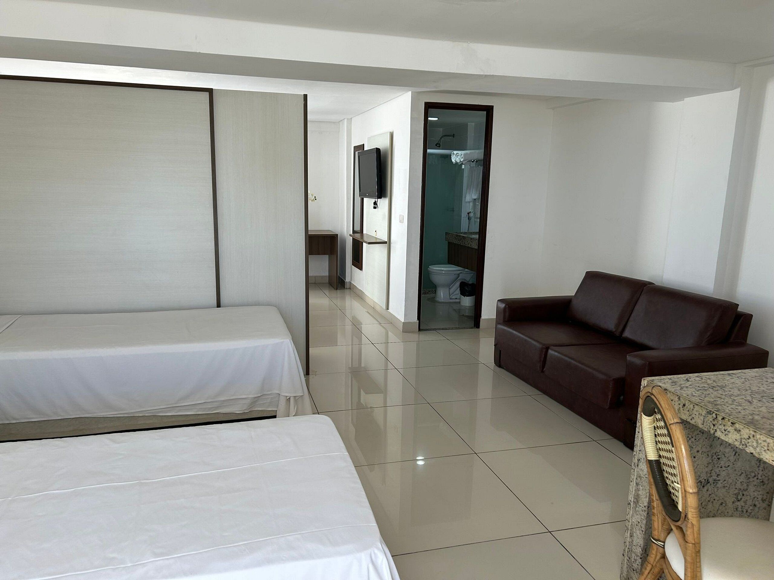 A hotel room with a bed, a sofa, a dining table, and a bathroom visible through an open door.