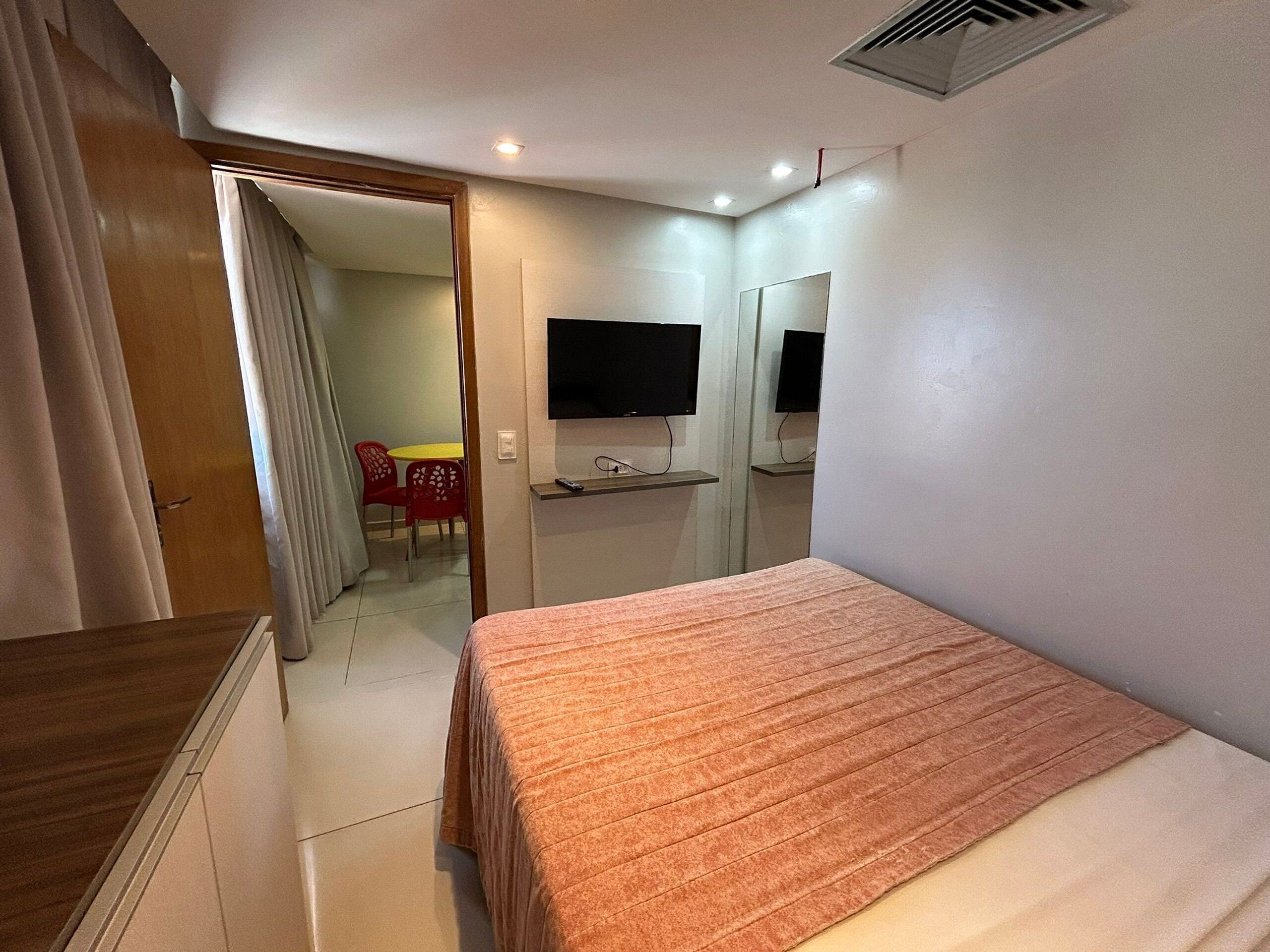A hotel room with a bed, a TV mounted on the wall, a desk, and a chair.