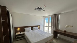 A hotel room with a bed, bedside tables, a nightstand, a desk, a window with curtains, and a view of the outside. - BELA HOSPEDAGEM-Imperial Flats em Tambaú (João Pessoa)