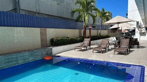 A swimming pool with tiled edges, lounge chairs, and a palm tree. - BELA HOSPEDAGEM-Imperial Flats em Tambaú (João Pessoa)