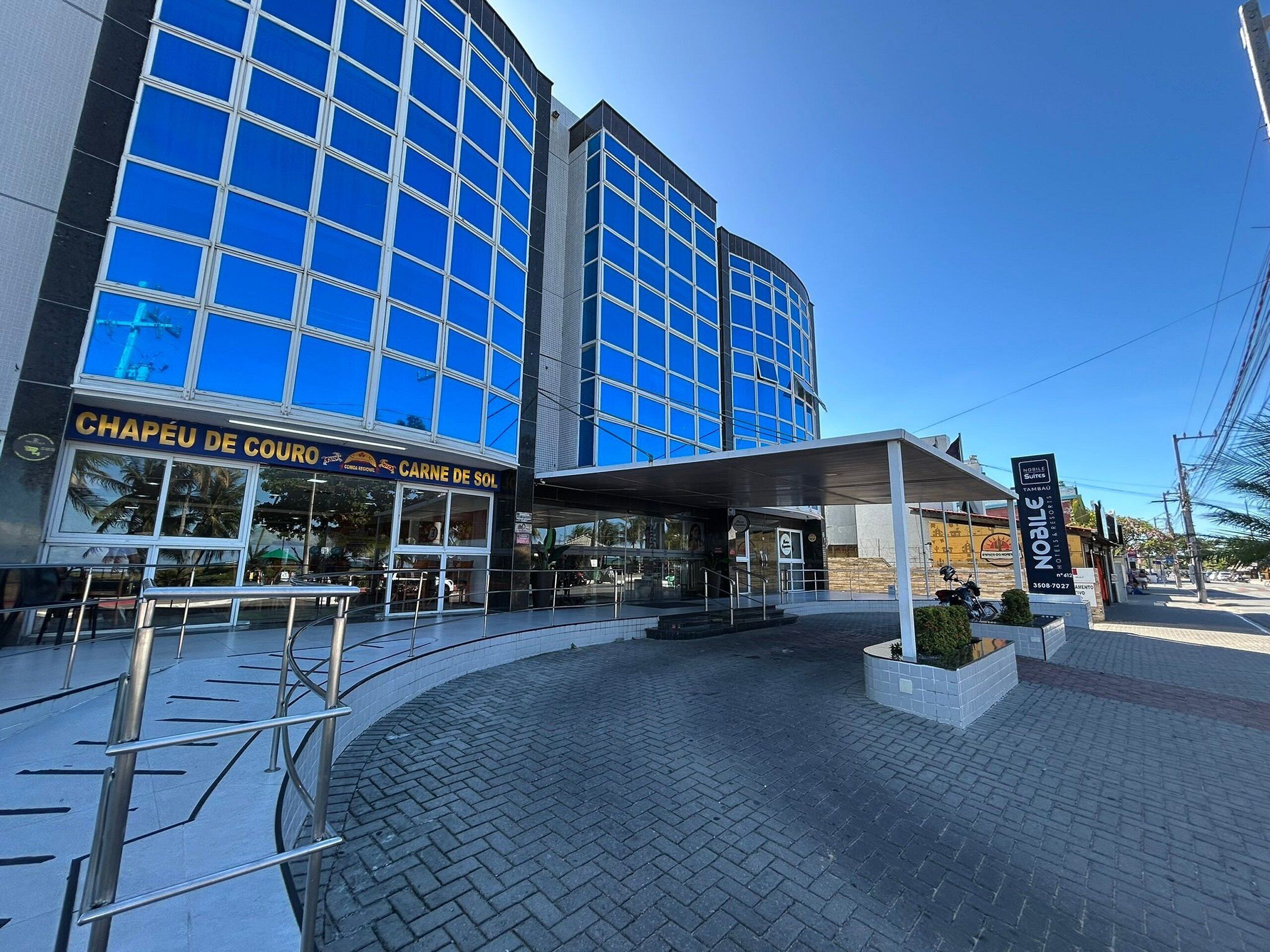 A modern building with a glass facade, a covered entrance, and a sign for 'CHAPÉU DE COURO'.