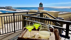 A balcony with a view of the sea, a lifeguard tower, and a tray with drinks. - Bright Corner Unit with Stunning Gulf Views & Sunsets (Destin)