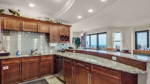 A spacious kitchen with granite countertops, wooden cabinets, and a built-in dishwasher. - Bright Corner Unit with Stunning Gulf Views & Sunsets (Destin)