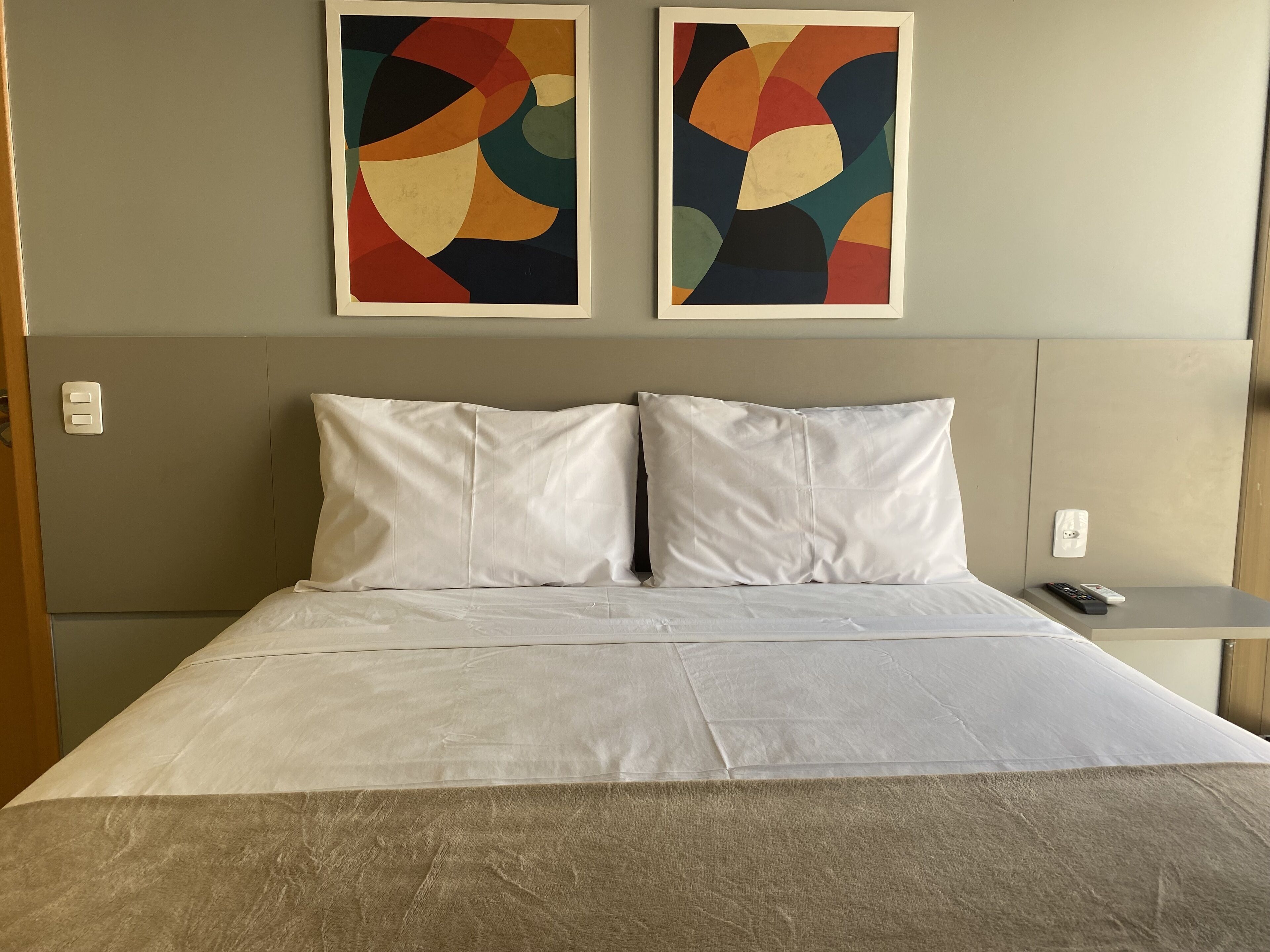 Hotelkamer met een bed, twee kussens, een nachtkastje en twee abstracte schilderijen aan de muur.