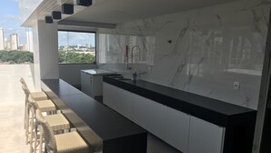 Een moderne keuken met een marmeren spatwand, een lange aanrecht en een ingebouwd spoelbak. Er staan rieten stoelen langs het aanrecht en een raam biedt uitzicht op de stad.